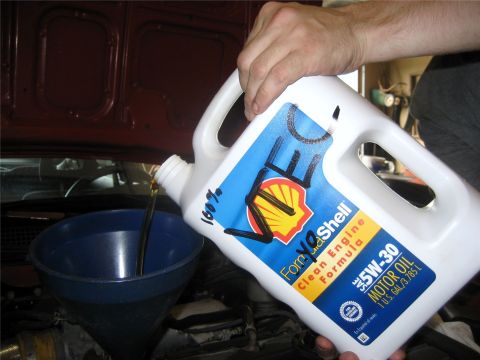 1993 Ford Probe - A person is pouring oil from a white jug into a blue funnel positioned over a car engine. The jug has a Shell oil label that reads '5W-30 M…