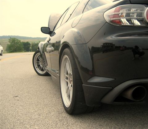 1993 Ford Probe - The rear quarter panel and wheel of a black sports car are shown from a low angle. The car has a wide stance and a visible exhaust pipe.