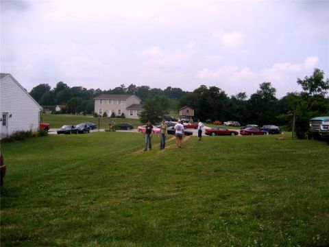 1993 Ford Probe - A group of people stand in a grassy yard with several cars parked in the background. A red pickup truck is parked to the left of a white ho…