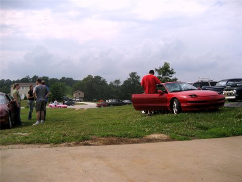1993 Ford Probe - A red Ford Probe is parked on a grassy area with its driver's side door open. Several people are gathered around the car and in the backgro…