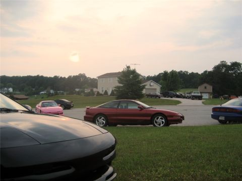 1993 Ford Probe - A red Ford Probe is parked on a grassy area next to a blue Ford Probe. In the background, several houses and trees are visible under a hazy…