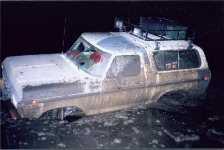 1991 Ford Bronco - This vehicle is deeply stuck in mud and water, with its tires submerged and the body covered in dirt.