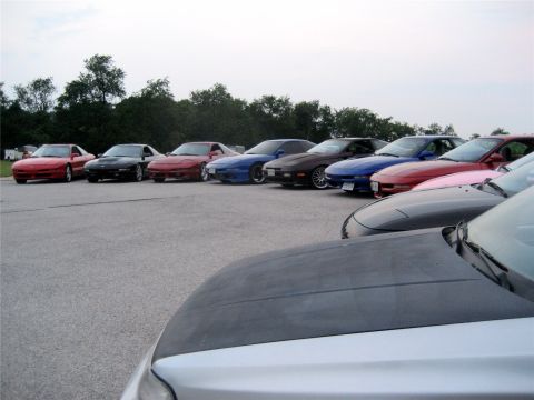 1993 Ford Probe - A line of several Ford Probe sports coupes are parked in an outdoor lot. The cars are various colors including red, black, blue, and pink,…
