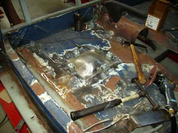 Welded bare-metal blister on a blue firewall panel surrounded by panel-beating tools