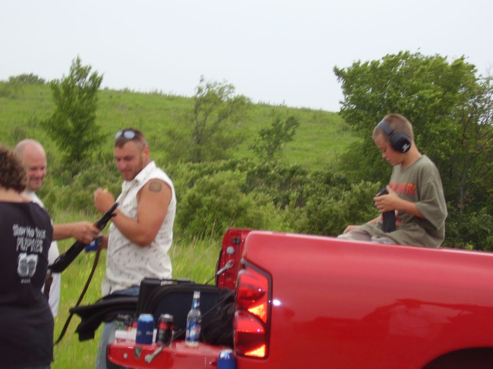 Red Ford F-150 truck bed with people and firearms outdoors.