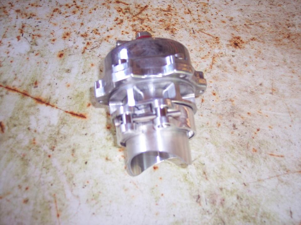 Chrome automotive part, possibly a blow-off valve, on a rusty surface