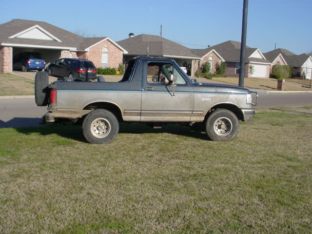 Two-tone Ford Bronco with top removed parked on grass in a residential street