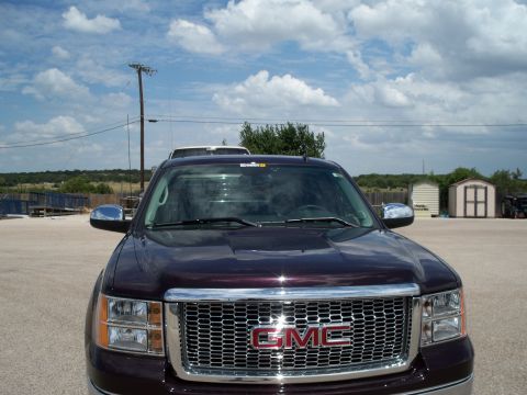 1996 Ford Bronco - A front-facing view of a dark purple GMC truck parked in a gravel lot with a blue ramp and utility poles in the background.