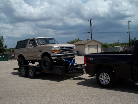 1996 Ford Bronco - A tan Ford Bronco is loaded onto a trailer being towed by a black pickup truck. The Bronco has a soft top and appears to be lifted.