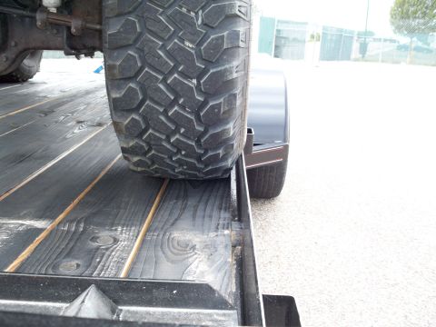 1996 Ford Bronco - A close-up view shows the tread of a large off-road tire resting on a dark wooden trailer deck. The tire is mounted on a vehicle, with susp…