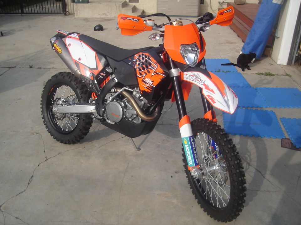 Orange and white KTM enduro dirt bike with handguards parked on concrete driveway
