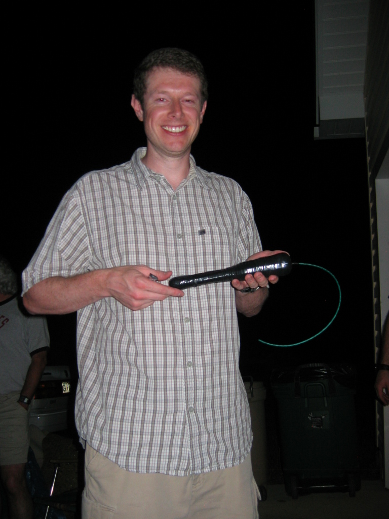 man holding a long object outdoors at night near trash cans