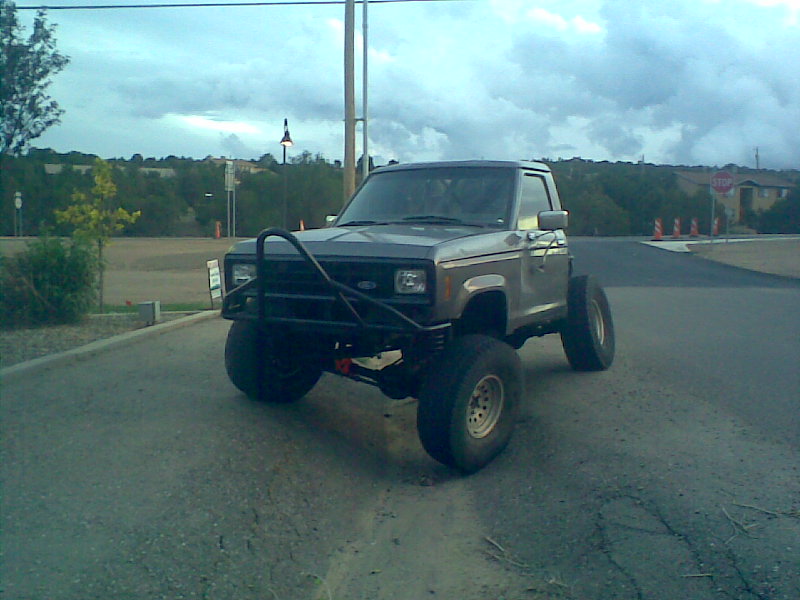 1984 Ford Bronco II with custom bumper and large tires, parked on a road.