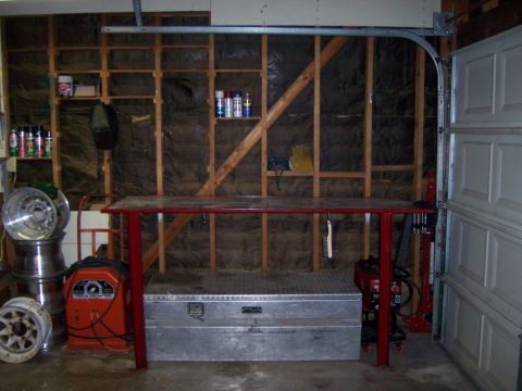 1991 Ford Bronco - Photograph of a fabricated red workbench in a garage with a welder, toolbox, and stacked wheels.