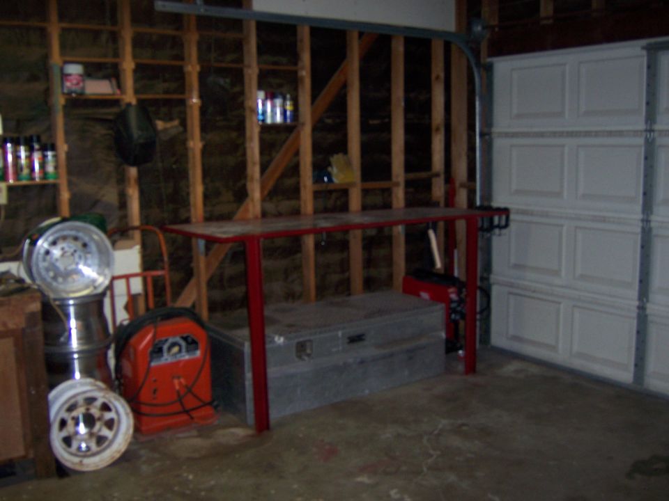 Red welded steel workbench in a garage beside a welder and chrome wheels