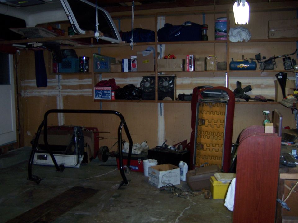 Garage interior with a roll cage in the foreground, shelves stocked with items, and a car seat leaning against a wall
