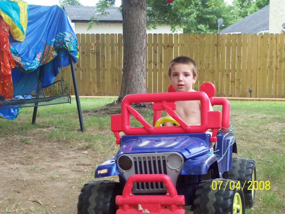 Toy jeep with red roll cage and blue body, driven by a young boy
