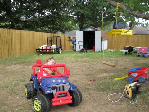 1994 Ford Bronco - A child sits in a blue and red toy jeep in a backyard, with other toys and a swing set visible.