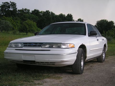 1996 Ford Crown Victoria - This white Ford Crown Victoria sedan is shown from a 3/4 front angle, parked outdoors on a dirt path.