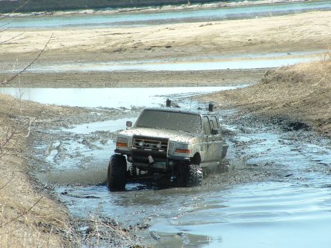 1992 Ford F-350 - A 1992 Ford F-350 navigates a muddy terrain, kicking up water and mud.