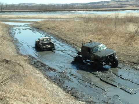 1992 Ford F-350 - Two trucks are navigating a difficult muddy terrain, with one assisting the other.
