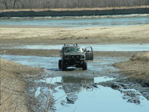 1992 Ford F-350 - A heavily modified pickup truck navigates a muddy, watery terrain with its driver's door ajar.