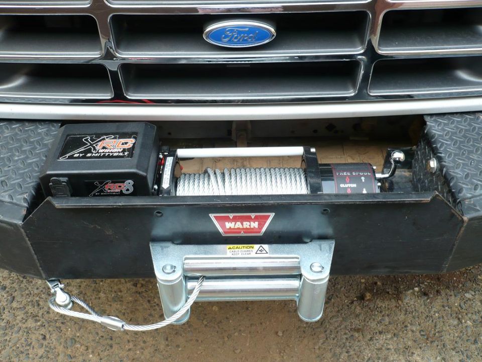 WARN winch with steel cable and Smittybilt XRC8 box in black bumper below a Ford grille emblem.