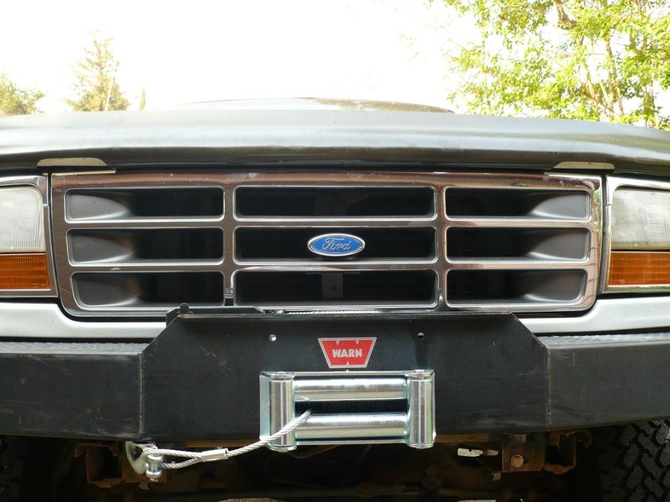 1992 Ford Bronco front grille with chrome bars and Ford logo, above a black bumper with a Warn winch