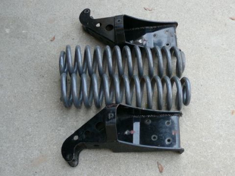 1988 Ford Bronco - Two removed front coil-spring buckets/shock towers laid on a concrete driveway, their black-painted stamped-steel brackets pointing in oppo…