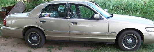 Gold 2000 Mercury Grand Marquis sedan, side view, parked on grass and dirt