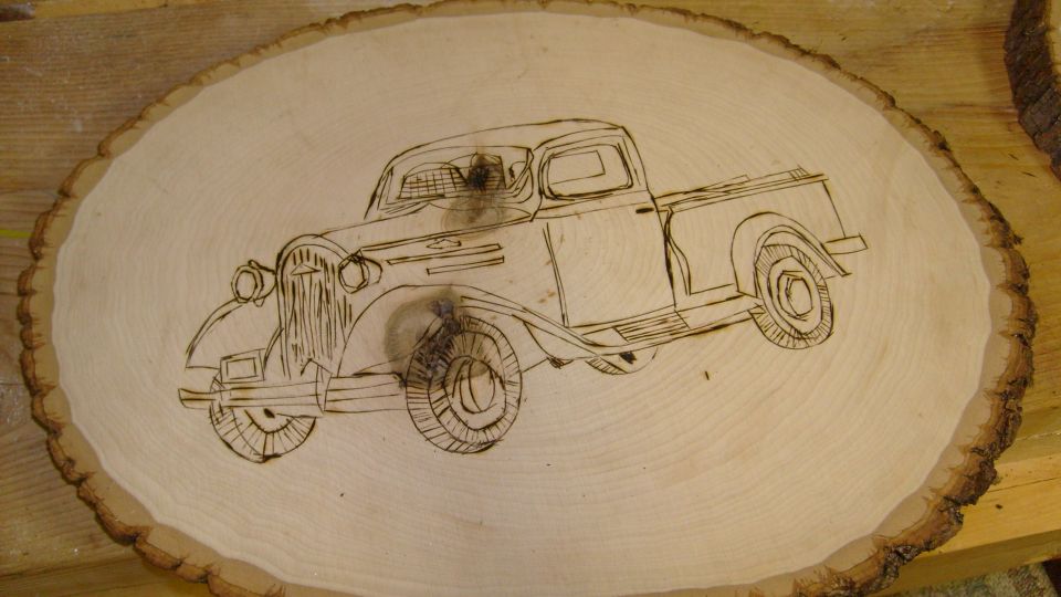 Wood-burned artwork of a 1930s pickup truck on a bark-edged wood slab