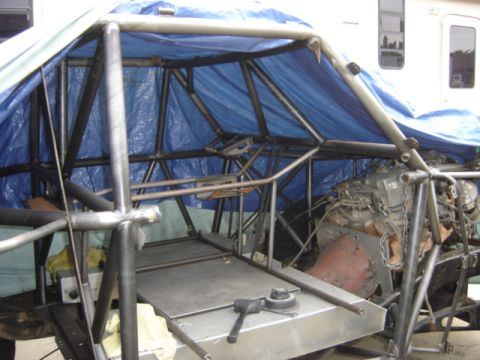 1995 Ford Bronco - A custom-built off-road vehicle is partially covered by a blue tarp, revealing its internal roll cage and engine components.