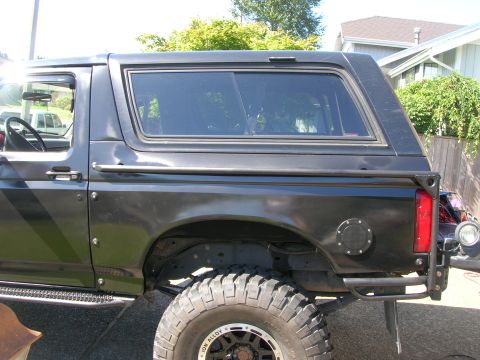 1996 Ford Bronco - Side view of a black SUV with large off-road tires and custom rear bumper.
