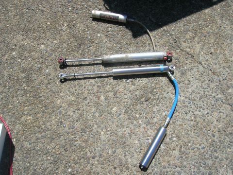 1996 Ford Bronco - Two shock absorbers, one with a blue hose, are placed on a textured surface.