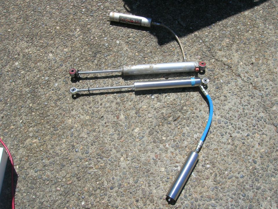 two shock absorbers and a remote reservoir laid out on asphalt
