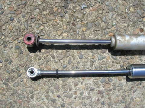 1996 Ford Bronco - Two automotive shock absorbers are laid out on a textured, pebbly surface.