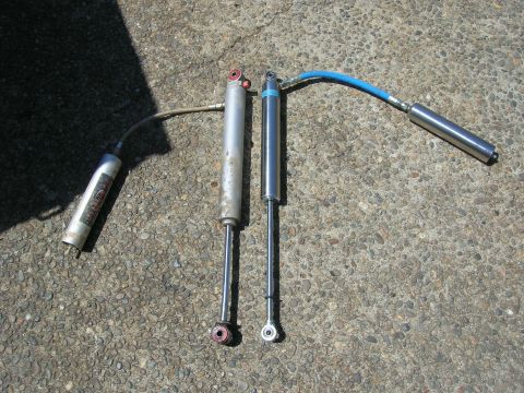 1996 Ford Bronco - Two shock absorbers are shown on a concrete surface, one with a remote reservoir and a blue hose.