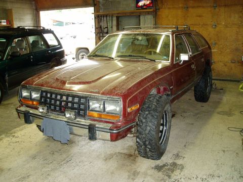 2000 Ford E350 - This AMC Eagle wagon, modified with large off-road tires, is parked indoors.