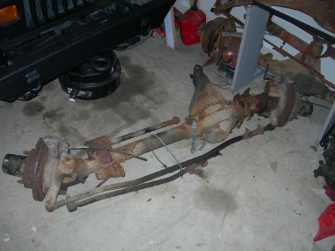 1985 Ford Bronco - Rusty front axle assembly, likely for an older 4x4 vehicle, shown on a garage floor.