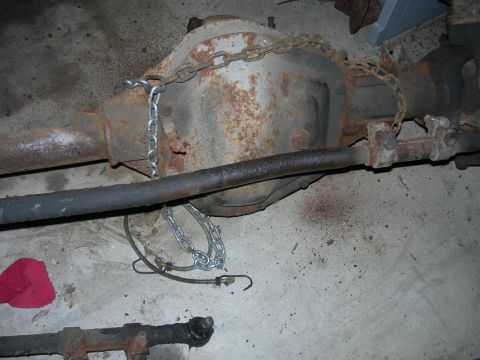 1985 Ford Bronco - Close-up of a rusty rear differential assembly with suspension components and chains.