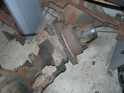 1985 Ford Bronco - Close-up view of a rusty front axle assembly, including a brake rotor and suspension parts.