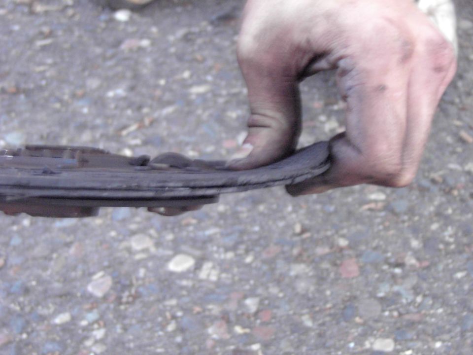 Hand holding a worn brake pad with visible metal backing