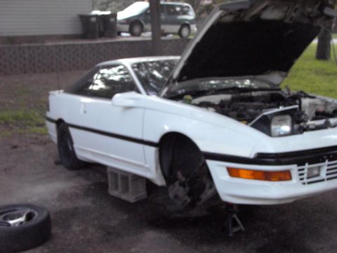 1991 Ford Probe - This white coupe is undergoing maintenance with its hood open and a wheel removed.