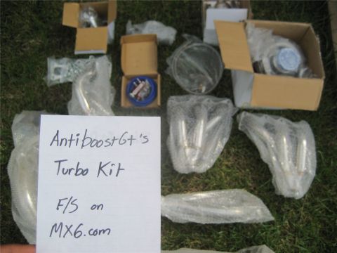 1993 Ford Probe - Various turbocharger components and exhaust manifolds are displayed on grass, accompanied by a handwritten note indicating they are for sal…