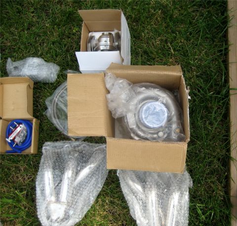 1993 Ford Probe - Unboxed turbocharger, blow-off valve, and other engine parts arranged on a lawn.