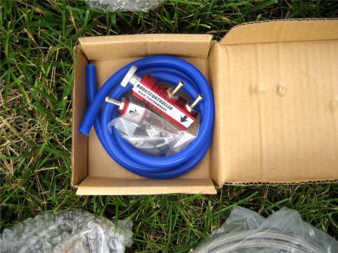 1993 Ford Probe - A red manual boost controller with blue tubing and hose clamps is neatly arranged inside a cardboard box, resting on green grass.