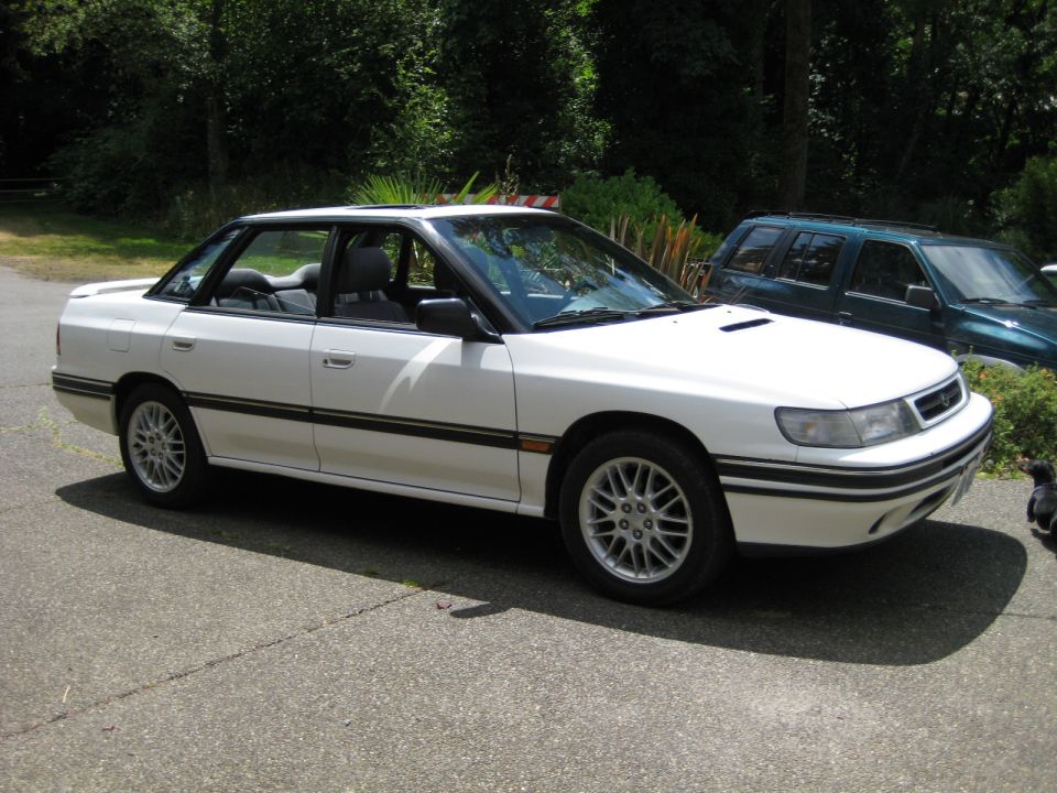 White four-door sedan parked on driveway, dark green SUV in background.