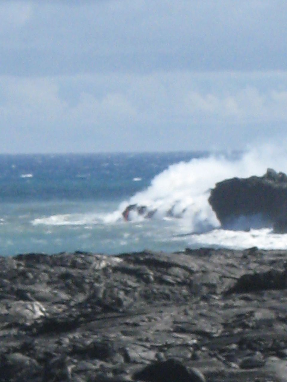 Volcanic coastline with waves crashing and steam rising.