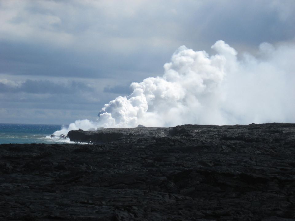 Steam rising from lava meeting the ocean on a rocky coast.