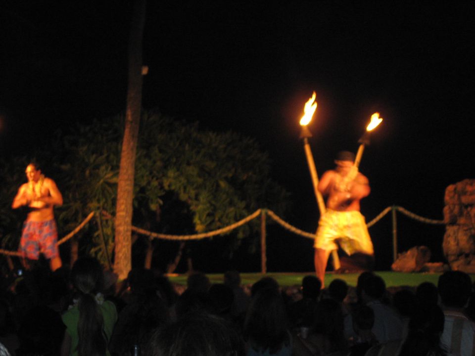 Two men perform with torches during a luau at night, with an audience watching